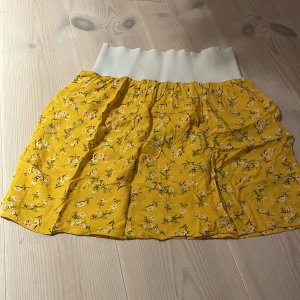 Gul blommig kjol - Superfin gul kjol med blommigt mönster, perfekt för sommardagar! Den har en bekväm vit resår i midjan som gör den lätt att bära. Kjolen är luftig och har en härlig sommarkänsla. Passar perfekt till en dag på stranden eller en picknick i parken. 🌼