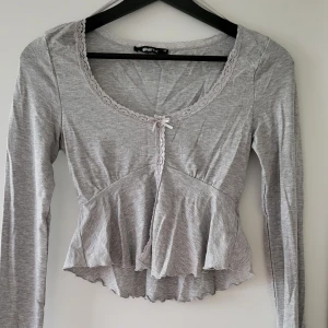 Grå långärmad topp från Gina Tricot - Säljer en superfin grå långärmad topp från Gina Tricot i storlek XS. Den har en söt spetsdetalj runt halsen och en liten rosett framtill. Endast använd 1 gång. Storlek: XS  Skickas inslagen i silkespapper i vattentätt paket.   Skicka pm för fler bilder. 