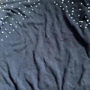 Svart tröja med pärlor från Bodyflirt - Säljer en snygg svart tröja från Bodyflirt i storlek M. Tröjan är dekorerad med vita pärlor över axlarna och har en mjuk och bekväm känsla. Perfekt för både vardag och fest!❤️