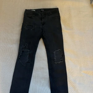 Svarta skinny jeans från Jack & Jones - Säljer ett par svarta skinny jeans från Jack & Jones i modellen Liam. De har en cool distressed look med slitningar på benen. Perfekta för en avslappnad men stilren outfit. Passar bra till både vardag och fest!