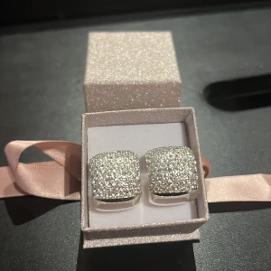 Glittriga örhängen i silver - Säljer ett par superfina glittriga örhängen i silver. De är fyrkantiga och täckta med små gnistrande stenar som verkligen fångar ljuset. Perfekta för en fest eller en speciell kväll. Kommer i en söt glittrig presentask med rosa rosett. Perfekt som present eller för att skämma bort dig själv! ✨Helt oanvända, från Edblad, kommer med fin förpackning💕Köpta för 499kr