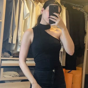 Svart oneshoulder topp - Snygg svart oneshoulder topp i tight passform. Perfekt för en utekväll eller fest. Den är ärmlös och har en stilren design som passar till både jeans och kjol.