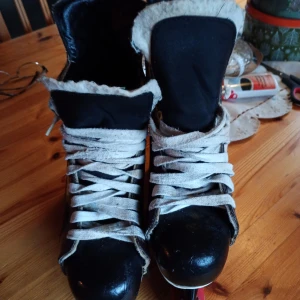Svarta och bruna skridskor från Bauer stl 39-42 - Säljer ett par klassiska svarta och bruna skridskor från Bauer. De har en robust design med vita snören och är perfekta för vinterns isäventyr. Skridskorna är i bra skick och redo för nya äventyr på isen!