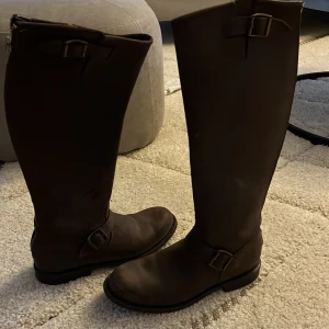 Bruna läderstövlar från Primeboots - Säljer ett par snygga bruna läderstövlar från Primeboots. De har en klassisk design med spännen upptill och vid ankeln. Perfekta för höst och vinter, och de ger en stilren look till vilken outfit som helst. Stövlarna är i mycket bra skick och redo för nya äventyr!