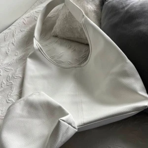Vit axelväska i skinn - Säljer en stilren vit axelväska i skinn. Den har en enkel och modern design med en bred axelrem som gör den bekväm att bära. Perfekt för både vardag och festliga tillfällen. Väskan är i mycket bra skick och redo för en ny ägare! Köptes för 1,600 säljer för 800 (kan diskuteras) 