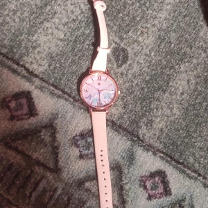 Vit klocka med blommig urtavla - Säljer en stilren klocka med vit rem och en vacker blommig urtavla. Klockan har romerska siffror och en elegant design som passar perfekt för både vardag och fest. Remmen är justerbar för bästa passform. Perfekt accessoar för att lyfta din outfit! 🌸