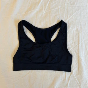 Svart sporttopp från Lindex - Säljer en svart sporttopp från Lindex i storlek 158/164 men passar perfekt till S. Perfekt för träning med en bekväm passform och elastiskt material. Toppen har en klassisk design med breda axelband och en racerback för extra stöd.