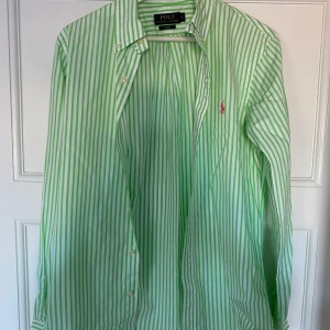 Grön och vit randig skjorta från Ralph Lauren - Säljer en snygg grön och vit randig skjorta från Ralph Lauren i slim fit. Skjortan har långa ärmar och knappar framtill. Perfekt för både vardag och festliga tillfällen. Den är i mycket bra skick och redo för en ny ägare!