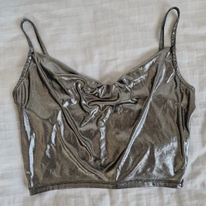 Festtopp H&M - Superfin silvrig festtopp från H&M! 🎀 Kort modell med vattenfallsrigning och justerbara axelband. Sparsamt använd, i perfekt skick!