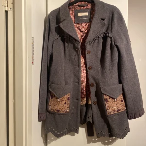 Grå kappa från Odd Molly - Säljer en superfin grå kappa från Odd Molly i ull. Den har snygga broderade detaljer och stora fickor med mönstrade kanter. Insidan är fodrad med ett färgglatt mönster. Perfekt för höst och vår! 🧥