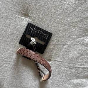 Brunt armband från Hultquist Copenhagen - Snyggt brunt armband från Hultquist Copenhagen med en flätad design. Armbandet har justerbara snören och silverfärgade detaljer. Perfekt accessoar för både vardag och fest. Nytt och oanvänt med etikett kvar. Helt nytt!