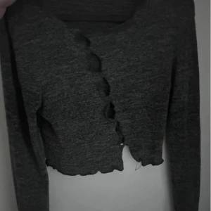 Grå ribbad croppad tröja - Säljer en snygg grå ribbad tröja med coola cut-out detaljer framtill. Den är croppad och har långa ärmar, perfekt för en trendig look. Passar bra till både vardag och fest! 🖤