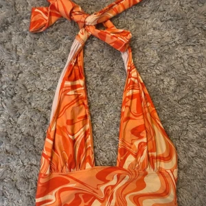 Orange mönstrad halterneck topp - Säljer en superfin orange halterneck topp med ett coolt mönster i olika nyanser av orange och vitt. Toppen är croppad och har en knytning i nacken.