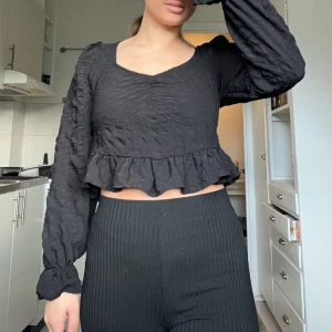 Svart långärmad blus med volang - Säljer en svart blus med långa ärmar och volangdetaljer. Den har en lös passform och är perfekt för höst och vår. Blusen är i mycket bra skick och passar både till vardags och fest.