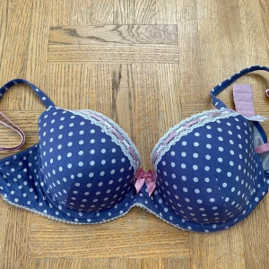 Blå prickig bh från Missya - Säljer en superfin blå bh med vita prickar från Missya. Den har söta spetsdetaljer och en rosa rosett framtill. Axelbanden är justerbara. Perfekt för att lägga till lite färg och mönster i garderoben! 💙