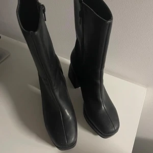 Svarta boots med klack - Snygga svarta boots i skinn med hög klack och dragkedja på sidan. Perfekta för höst och vinter, dessa boots ger en stilren look och är både bekväma och trendiga. Passar bra till både jeans och klänning.