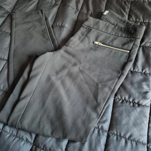 Svarta byxor från Gina Tricot - Snygga svarta byxor från Gina Tricot i storlek M. De är gjorda av polyester och viskos med en liten del elastan för stretch. Byxorna har en tight passform och coola dragkedjedetaljer på fickorna. Perfekta för både vardag och fest!