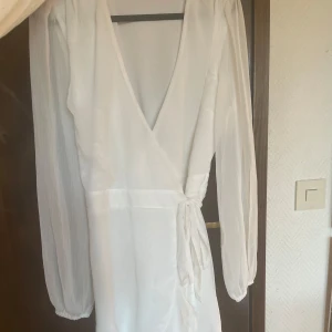 Vit omlottklänning från Bubbleroom - Säljer nu min älskade studentklänning från bubbleroom!! Super fin, knytningen i midjan är en så fin detalj och den går att knyta precis som man vill. Storlek 40, men passar dom som vanligtvis har 38 också. Inte så genomskinlig, jag hade beiga cykelbyxor under och de syntes ingenting🤩🥰endast använd en gång så skicket är som nytt. Köpt för 769kr✨