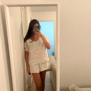 Vit blus med spetsdetaljer - Säljer en superfin vit blus med spetsdetaljer och korta ärmar. Blusen har en söt knytning framtill och ett luftigt, bekvämt linne  material. Jag köpte den i en lite söt affären i Italien 