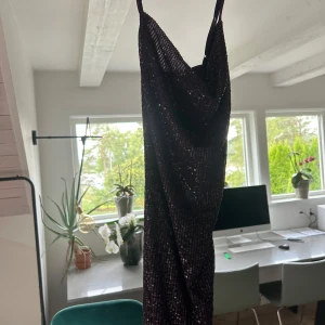 Mörklila paljettklänning - Säljer en superfin mörklila klänning med paljetter som ger en glittrig look. Klänningen är axelbandslös och perfekt för festliga tillfällen. Den har en elegant passform och är i nytt skick med etiketten kvar. Perfekt för nyår eller en glamorös kväll ute! Aldrig använd 