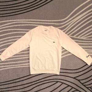 Vit sweatshirt från Lacoste - Säljer en stilren vit sweatshirt från Lacoste i storlek M. Tröjan har det klassiska krokodilemblem på bröstet och Lacoste-loggan broderad på ärmen. Perfekt för en avslappnad och snygg look. Passar både till vardags och lite finare tillfällen. 🐊✨