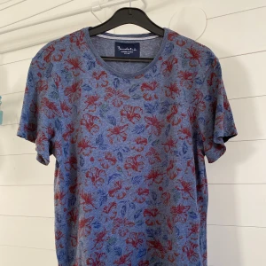 Blå blommig t-shirt från Bondelid - Säljer en snygg blå t-shirt från Bondelid med ett blommigt mönster i rött och blått. Den är kortärmad och i fint skick. Passar alla tillfällen 🌸