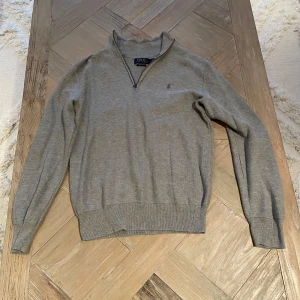 Grå tröja från Polo Ralph Lauren - Säljer en stilren grå tröja från Polo Ralph Lauren i mjuk pima bomull. Tröjan har en dragkedja vid halsen och långa ärmar. Perfekt för både höst och vår, och funkar lika bra till vardags som till lite finare tillfällen.