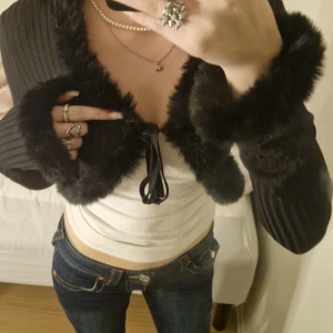 Svart bolero med pälsdetaljer - Säljer en superfin svart bolero med pälsdetaljer på krage och ärmslut. Den är perfekt för att ge en extra touch till din outfit. Jackan har långa ärmar och knyts framtill. Passar perfekt för höst och vinter. Perfekt för festliga tillfällen! 🖤