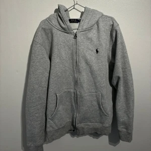 Grå hoodie från Polo Ralph Lauren - Säljer en klassisk grå hoodie från Polo Ralph Lauren i mycket bra skick. Den har en dragkedja framtill och en liten broderad logga på bröstet. Perfekt för höst och vår, med en skön passform och praktiska fickor. Huvan ger extra mysfaktor!  Väldigt dålig dragkedja funkar knappt
