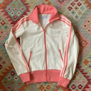 Vit och rosa jacka från Adidas - Säljer en snygg vit och rosa Adidas jacka i mycket bra skick. Klassiska tre ränder längs ärmarna och broderad logga på bröstet. Riktig y2k staple. Passar XS - S.
