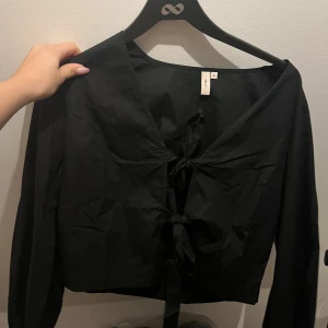 Svart långärmad topp med knyt - Säljer en stilren svart topp från Nelly med långa ärmar och snygg knytning framtill. Perfekt för både vardag och fest! 🖤 prislapp kvar , aldrig använd 