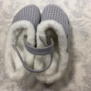 Grå tofflor med foder - Mysiga grå tofflor med vit fluffig foder. Perfekta för kalla dagar hemma. De har en perforerad ovansida och en justerbar rem för bättre passform.                                                   Stlk kvar 40,41,42 43 och 44                           Tjocka fleece inuti, rekommenderar att välja 2 Stlk större än som är vanlig i storlek. Till exempel storlek 43 passar som är Stlk 41 i vanligt storlek 