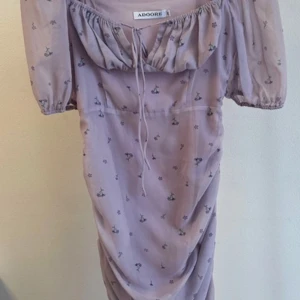 Ljuslila klänning från Adoore - Superfin ljuslila klänning från Adoore med små blommor. Den har en söt knytning framtill och puffiga kortärmar. Perfekt för vår och sommar! Något litet i storleken. Passar en 38.💜