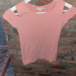 Rosa topp från Amisu - Säljer en söt rosa topp från Amisu i storlek S. Toppen har en unik design med öppna axlar och korta ärmar. Perfekt för sommardagar eller en avslappnad utflykt. Materialet är mjukt och bekvämt, vilket gör den idealisk för vardagsbruk.