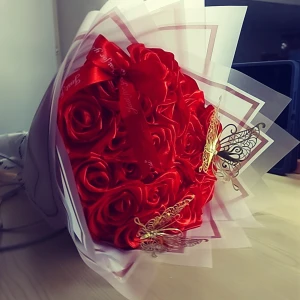 Röd rosformad bukett med fjärilsdetaljer - En vacker bukett med röda rosor i tyg, dekorerad med eleganta guldfärgade fjärilar. Perfekt som present eller dekoration för speciella tillfällen. Rosorna är inslagna i ett stilrent vitt papper med röda kanter och ett matchande rött band.