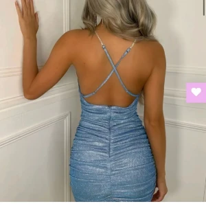 Glittrig blå klänning - Snygg glittrig blå klänning med smala axelband som korsas i ryggen. Perfekt för festliga tillfällen! Den har en tight passform och är kort, vilket ger en elegant look. Materialet är glittrigt. Storlek S