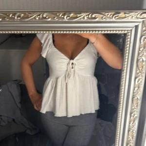 Vit topp med knytning - Säljer en söt vit topp med knytning framtill. Den har en luftig passform och korta ärmar, perfekt för sommardagar. Toppen är i bra skick och passar både till vardags och festliga tillfällen.