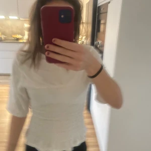 Vit smockad topp - Säljer en superfin vit smockad topp med trekvartsärm. Den har en söt volangdetalj vid nederkanten och är perfekt för både vardag och fest. Toppen är i mycket bra skick och passar perfekt till jeans eller kjol. Perfekt för vår och sommar!