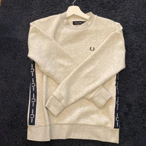Grå sweatshirt från Fred Perry - Säljer en stilren grå sweatshirt från Fred Perry i mycket bra skick. Tröjan har långa ärmar och ett klassiskt broderat Fred Perry-märke på bröstet. Perfekt för en avslappnad stil och passar till både vardag och träning. 🖤