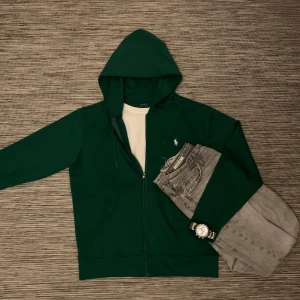 Grön hoodie från Ralph Lauren - Säljer en snygg grön hoodie från Polo Ralph Lauren i storlek S. Den har en dragkedja framtill och en klassisk logga på bröstet. Perfekt för en avslappnad stil och passar bra till både jeans och joggers. Huvan har snören för justering. Perfekt för höst och vår! Knappt använd då den inte riktigt passade min stil.