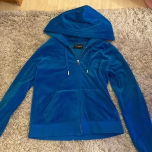Blå huvtröja från Juicy Couture - Snygg blå huvtröja från Juicy Couture med huva och dragkedja. Perfekt för en avslappnad stil. Jackan har långa ärmar och en bekväm passform.
