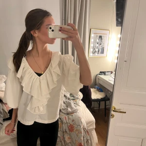 Vit blus med volangdetaljer - Säljer en elegant vit blus med v-ringad design och volangdetaljer. Blusen har trekvartsärmar och är perfekt för en stilren look. Passar bra till både jeans och kjol.