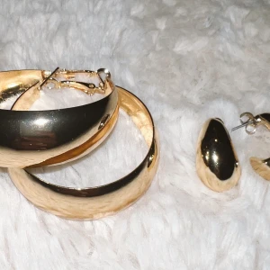 Guldiga örhängen  - Snygga och eleganta guldiga örhängen och matchande armband. Örhängena har en stilren design med en slät yta som ger en lyxig känsla. Armbandet är brett och har en enkel låsning. Perfekt för att piffa upp vilken outfit som helst, oavsett om det är till fest eller vardag.