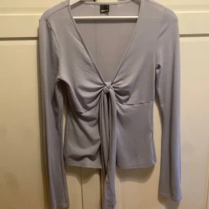 Ljuslila långärmad topp med knyt - Säljer en superfin ljus blå topp från Gina tricot. Den har långa ärmar och en snygg knytning framtill som ger en cool look. Perfekt för både vardag och fest! 😊