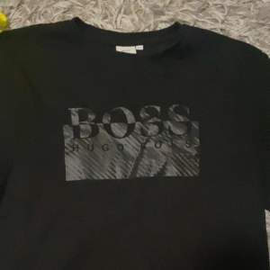 Snygg svart t-shirt från Hugo Boss med stort BOSS-tryck på framsidan. Perfekt för en stilren och avslappnad look. Passar både till vardags och fest. Materialet känns mjukt och skönt mot huden.