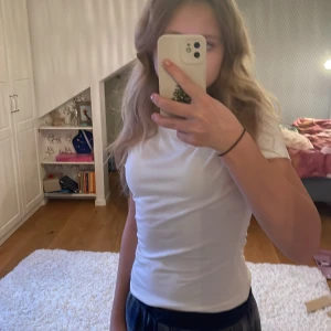 Vit tight t-shirt - Säljer en vit tight t-shirt i mycket bra skick. Perfekt basplagg för alla tillfällen. Den ärmlösa designen gör den idealisk för varma sommardagar eller som lager under en jacka.