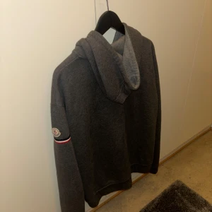 Grå hoodie från Moncler - Säljer en snygg grå hoodie från Moncler i bra skick. Den har en dragkedja framtill och en klassisk Moncler-logga på ärmen. Perfekt för höst och vinter, och den är supermjuk och bekväm. Passar både till vardags och chillkvällar. Hör av dig vid intresse!  Stolek xxl men är som en L