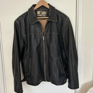 Svart skinnjacka - Snygg svart skinnjacka från Gato med dragkedja och klassisk krage. Det är en rejäl skinnjacka som också håller dig varm. Storlek M. 