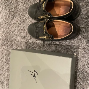 Svarta Giuseppe zanotti skor  - Snygga svarta sneakers från Giuseppe Zanotti med gulddragkedjor och logga. Skorna har en stilren design med snörning och är i mycket bra skick. Perfekta för både vardag och fest!