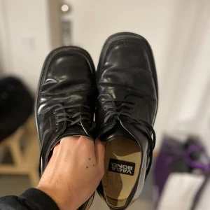 Svarta skinnskor från Vaga Bond - Snygga svarta skinnskor från Vaga Bond med klassisk snörning. Perfekta för en stilren look. Tillverkade i Portugal med läderöverdel och läderfoder.